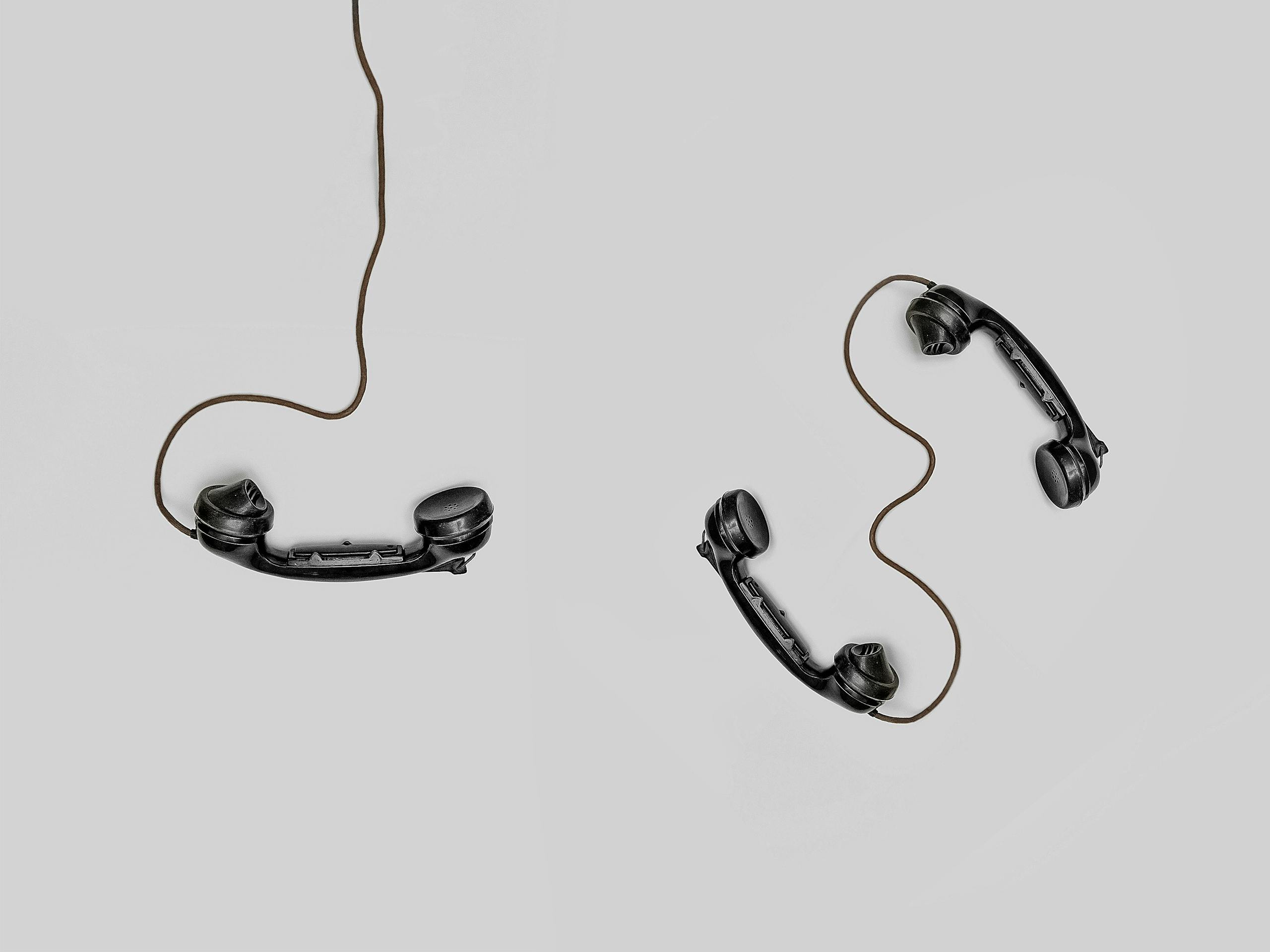 Two vintage black telephone handsets connected by cords on gray background.